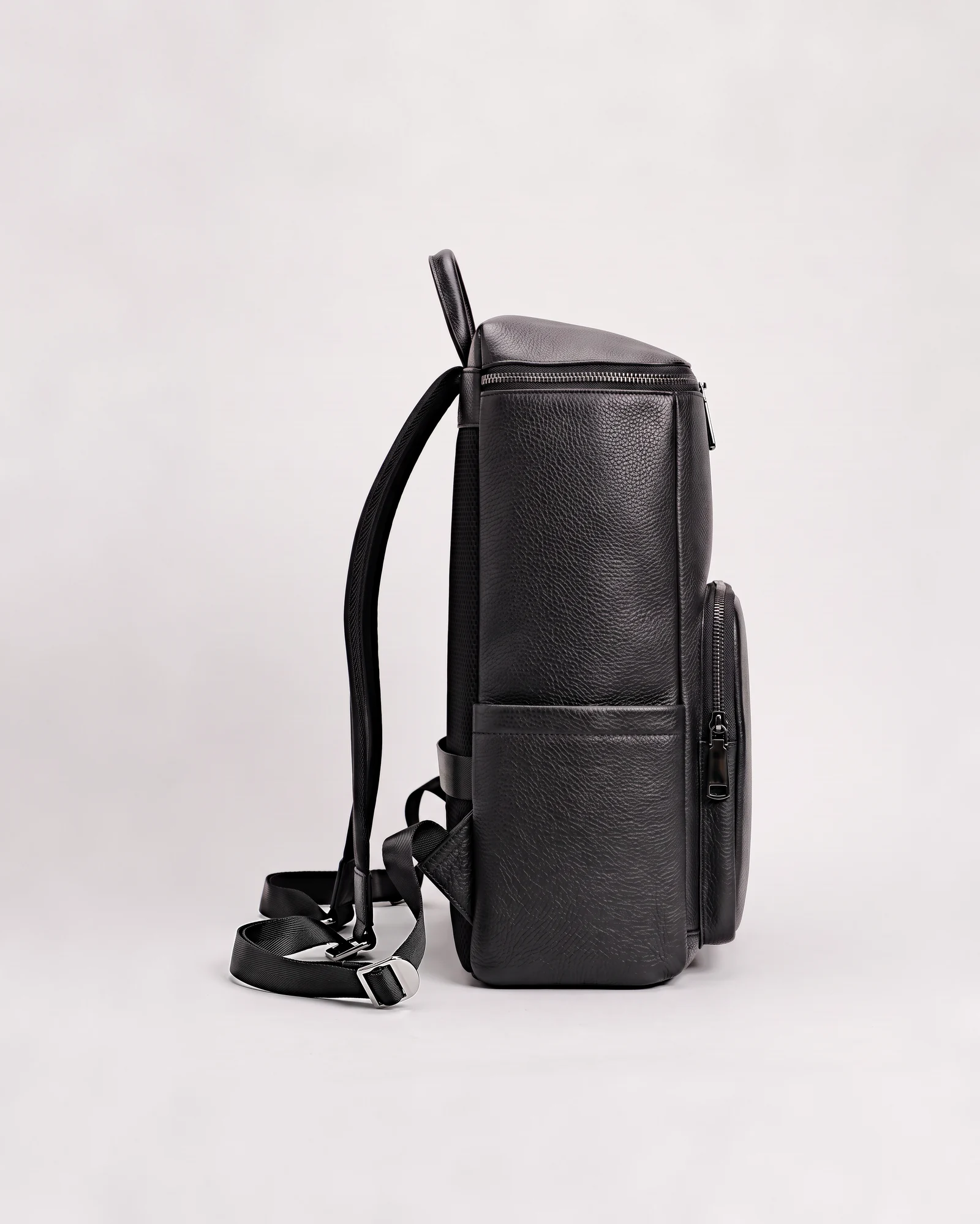 Profil gauche du sac LC/01 posé au sol sur fond gris clair, profondeur, zip de poche et poche latérale visibles